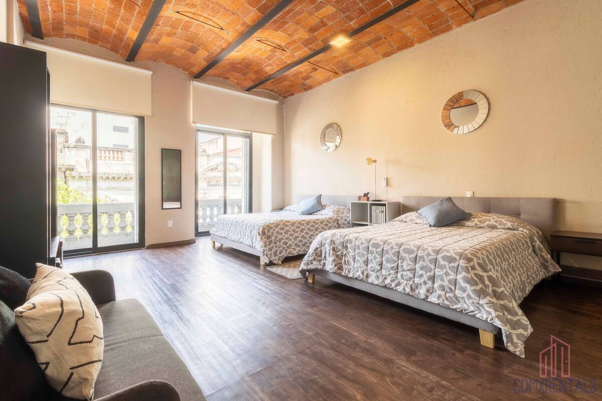 A modern bedroom with two beds, a sofa, and a large window.