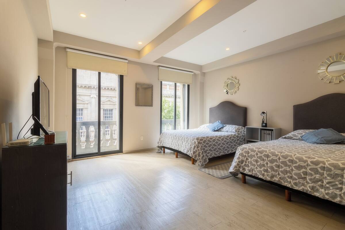 A spacious bedroom with two beds, large windows, and a balcony.