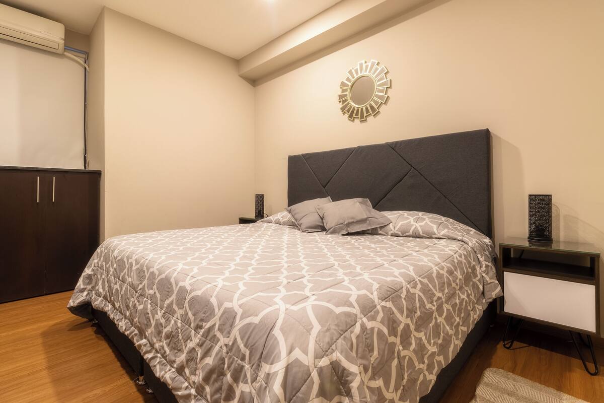 A bedroom with a bed, a nightstand, a dresser, a wall-mounted mirror, and a ceiling light fixture.