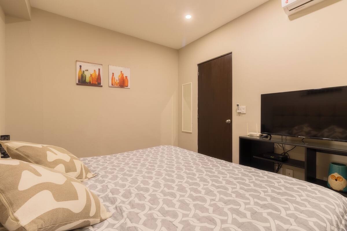 A bedroom with a bed, two pillows, a TV, and wall art.