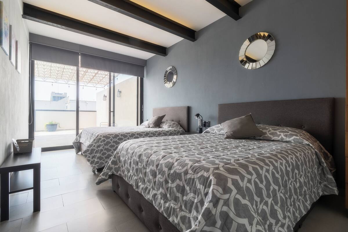 A modern bedroom with two beds, large windows, and decorative mirrors.