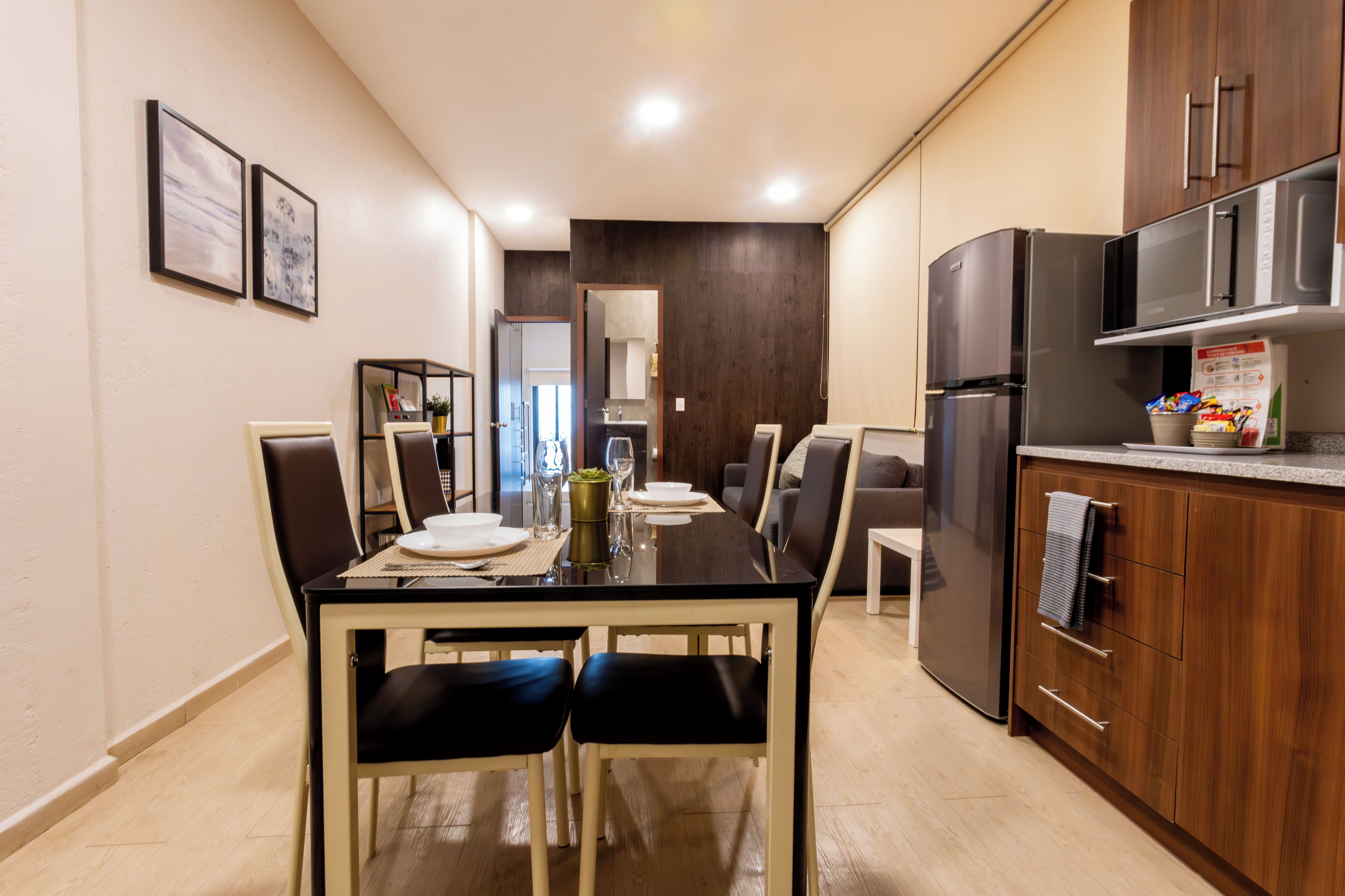 A modern kitchen with a dining area, featuring a refrigerator, microwave, and wooden cabinets.