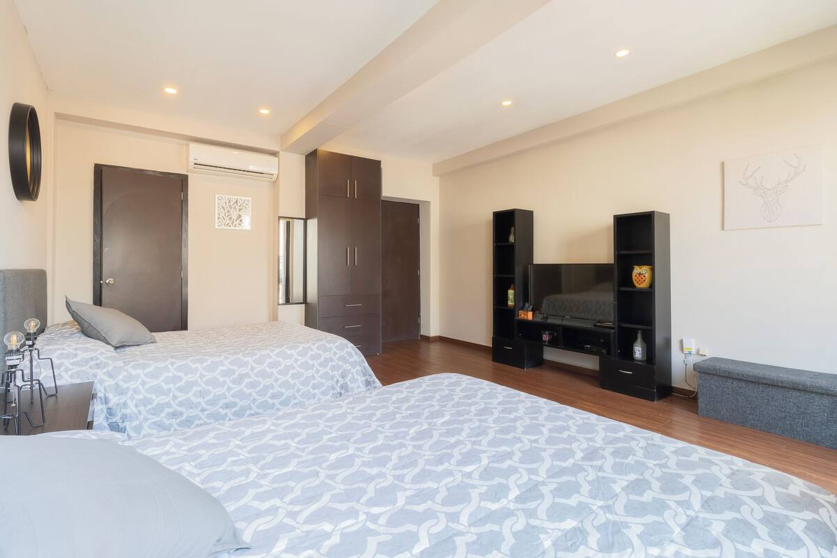 A hotel room with two beds, a wardrobe, a TV stand, and a wall-mounted artwork.