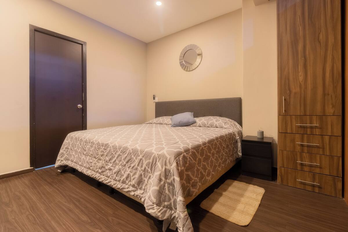 A bedroom with a bed, a nightstand, a wardrobe, and a wall clock.