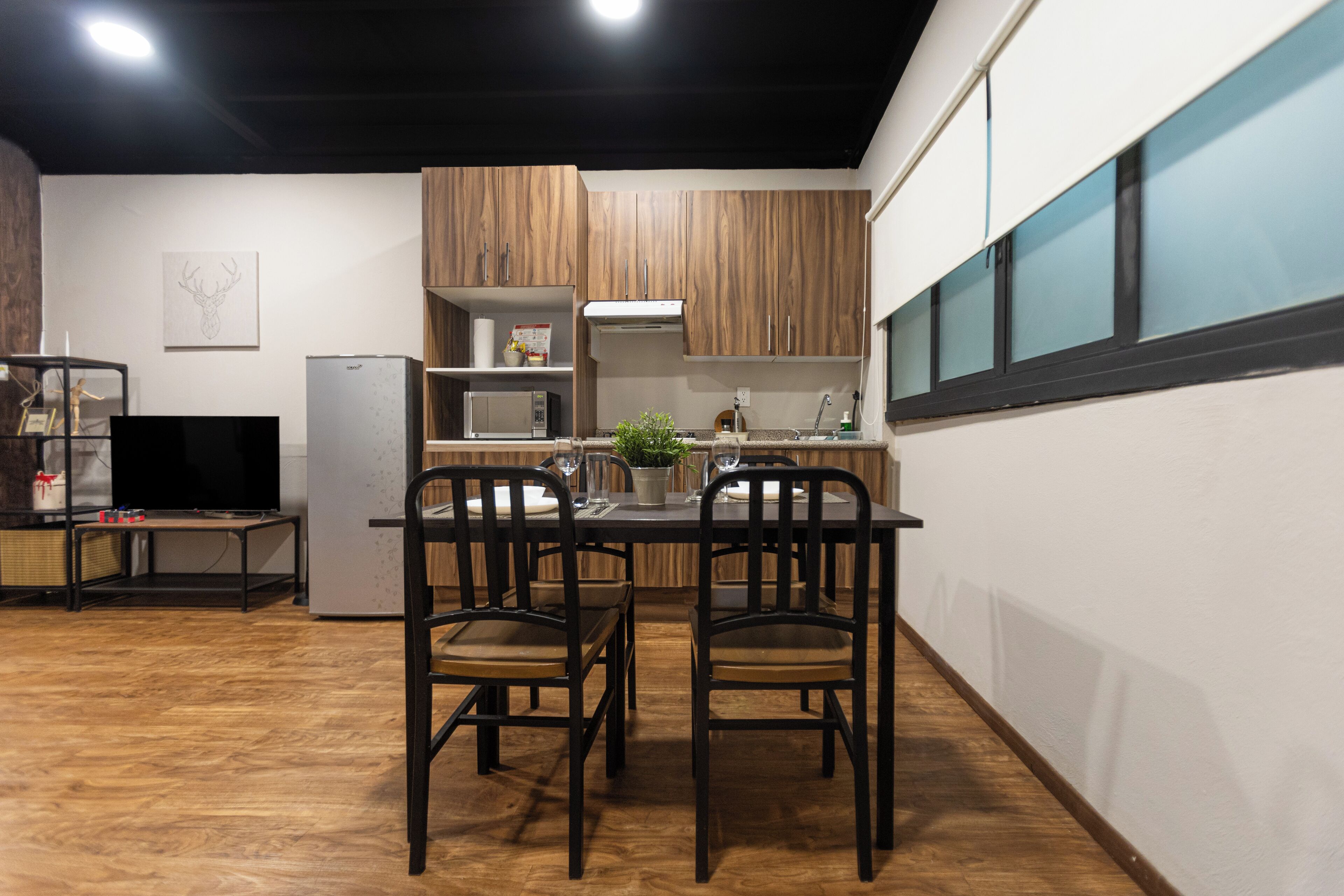 Una cocina moderna con armarios de madera, una mesa de comedor con sillas, un refrigerador y un microondas.