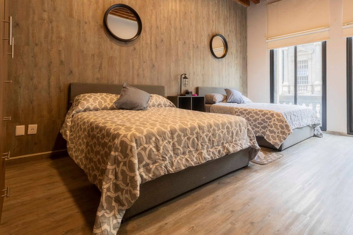 A bedroom with two beds, wooden walls, and a large window.
