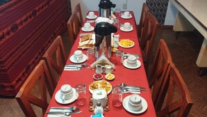 Ein Esszimmertisch ist gedeckt mit Tellern, Besteck und einer Kaffeekanne, umgeben von hölzernen Stühlen.