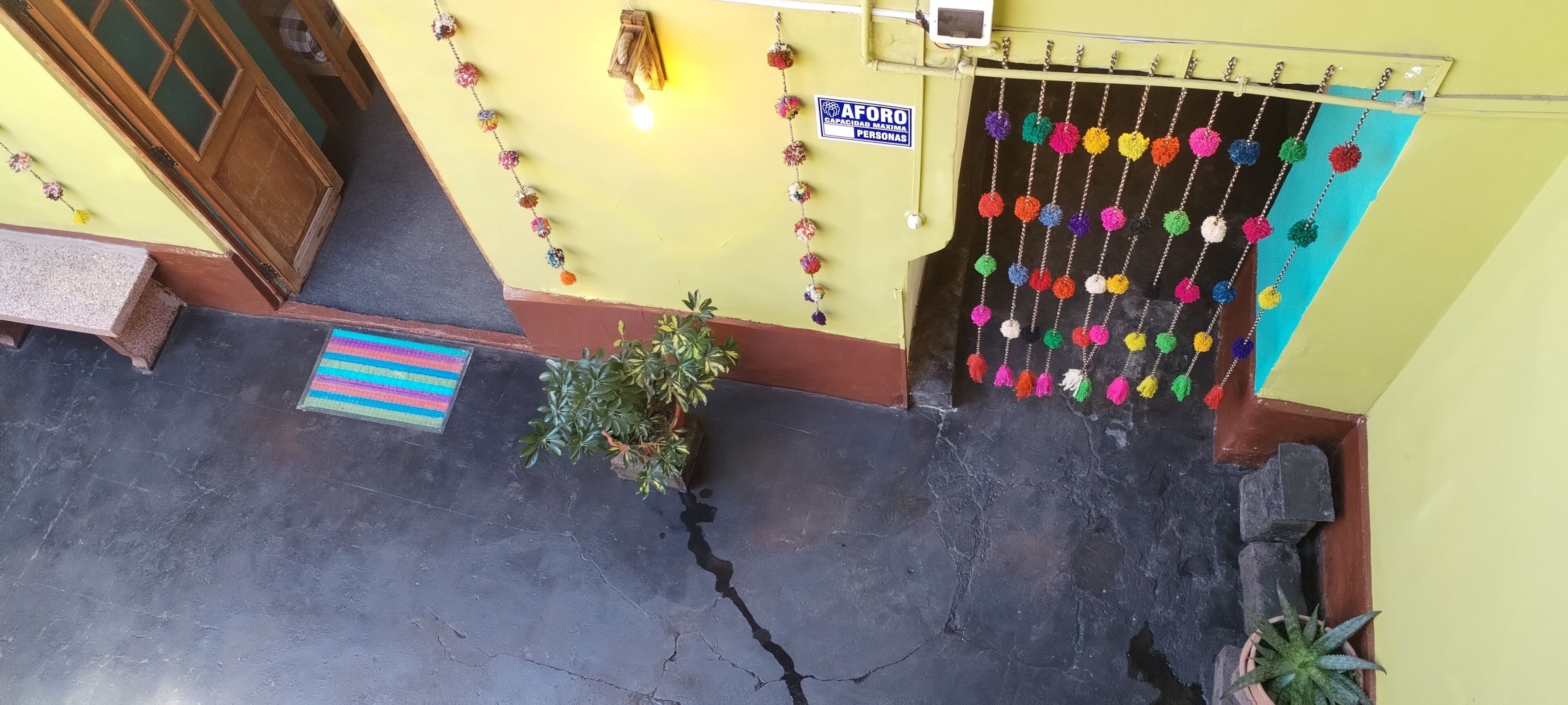 Entrada de hotel con pared amarilla, puerta de madera y un cartel que indica 'AFORO'.