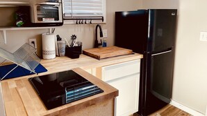 A compact kitchen with a black refrigerator, a wooden countertop, a built-in dishwasher, and a window with blinds.