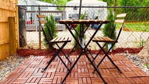 A patio area with a wooden table and two chairs, surrounded by a chain-link fence.