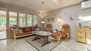 A cozy living room with a wooden ceiling, a leather sofa, a coffee table, and a wicker side table.