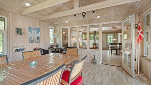 A spacious wooden interior with a large dining table, multiple chairs, and a view of the outdoors through glass doors.