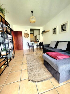 Ein Wohnzimmer mit einer Couch, einem Essbereich mit Stühlen, einer Küche im Hintergrund und einer Treppe mit einer Pflanze.