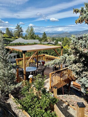 Eine Holzterrasse mit Gartenmöbeln, umgeben von viel Grün und mit Blick auf eine schöne Landschaft.
