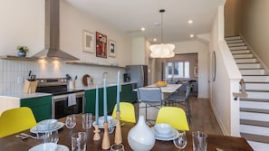 Une cuisine moderne avec un îlot central, un coin repas avec des chaises jaunes et un escalier menant à un autre niveau.