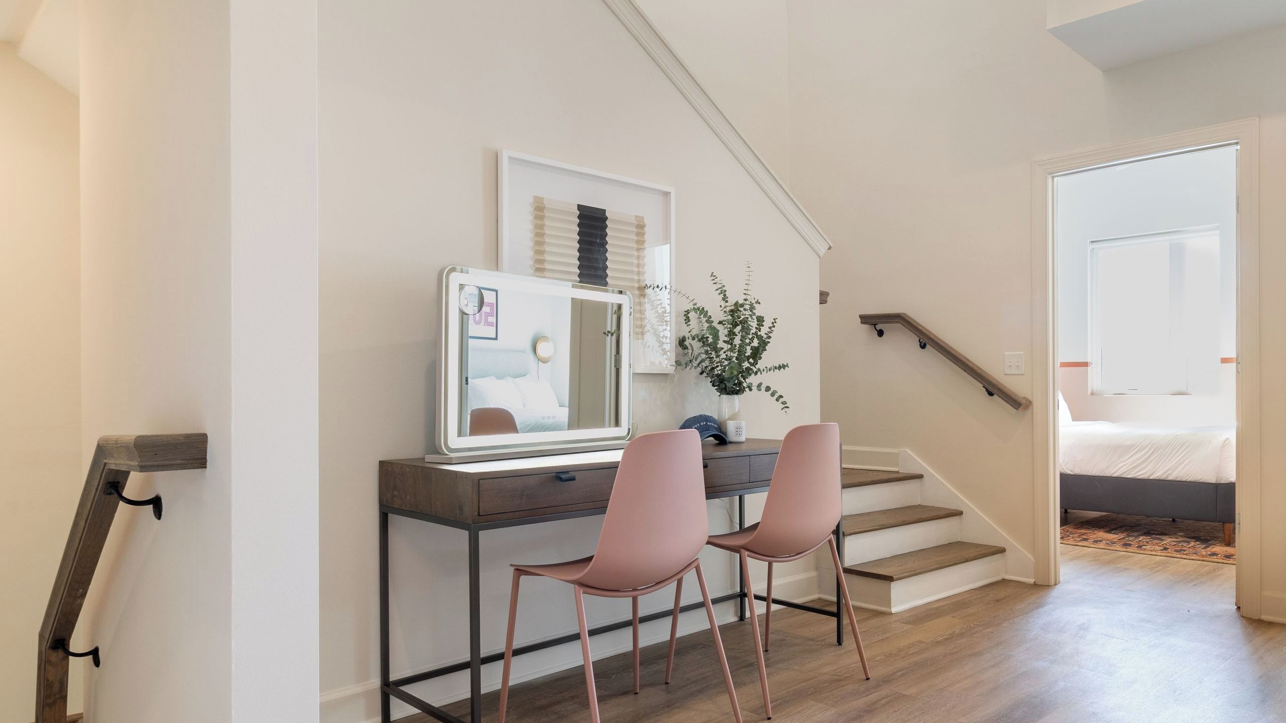 A modern room with a desk, two pink chairs, a mirror, and a staircase leading to another room.