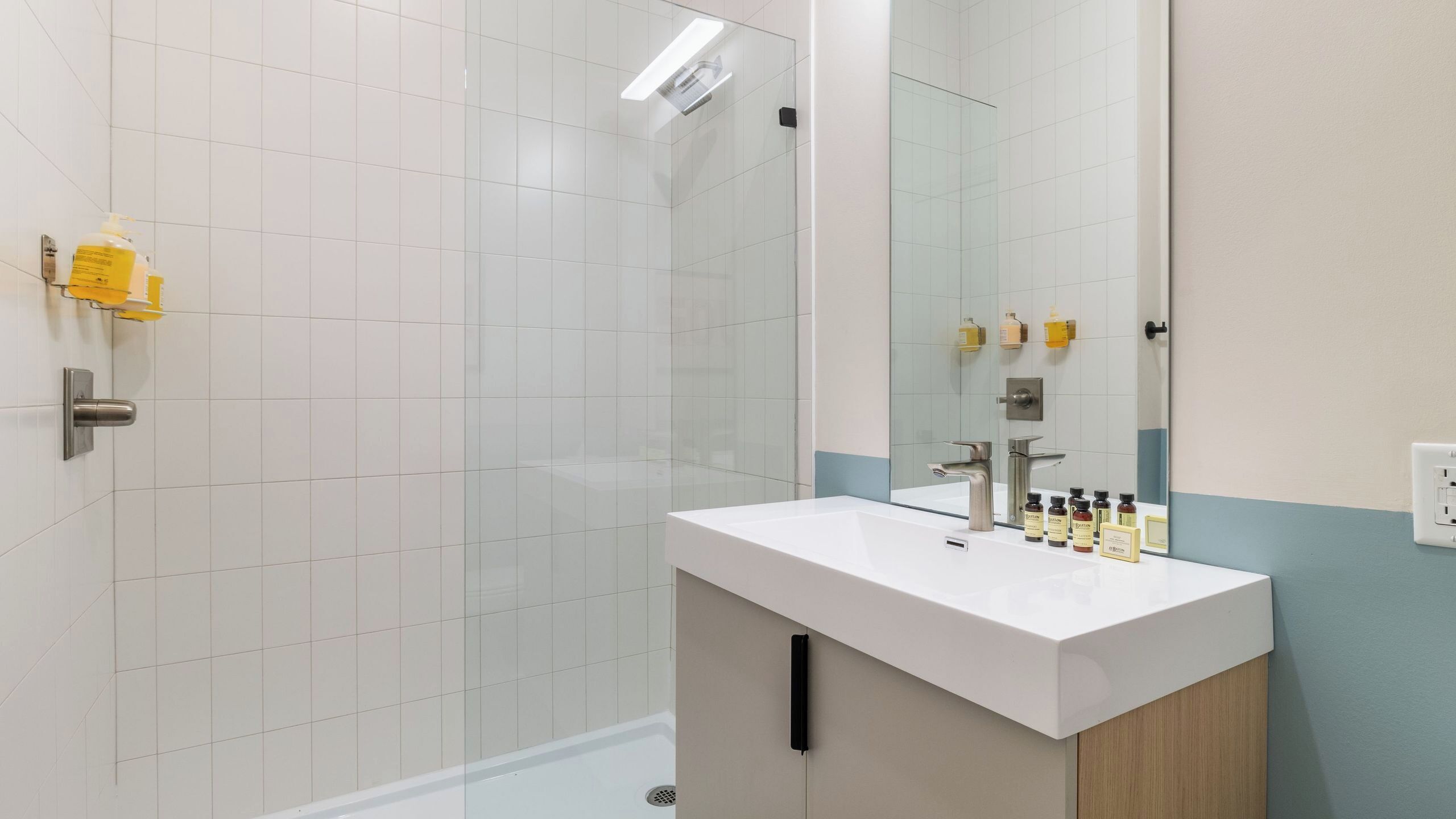 A modern bathroom with a glass shower enclosure, a white sink with a mirror, and toiletries on the countertop.