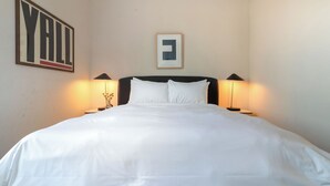 A neatly made bed with white linens, two bedside lamps, a framed picture above the bed, and a wall sign with the word 'YAIL'. - Conway Professionally Managed Buyout in DT Nash (Nashville)
