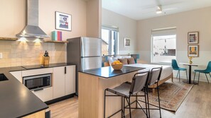 Eine moderne Küche mit Kühlschrank, Mikrowelle und Kaffeemaschine. Es gibt eine Essecke mit Tisch und Stühlen sowie ein Bett mit Blick auf die Stadt.