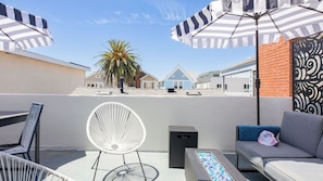 Une terrasse sur le toit, aménagée avec du mobilier d’extérieur, un palmier et une vue sur les bâtiments en arrière-plan.