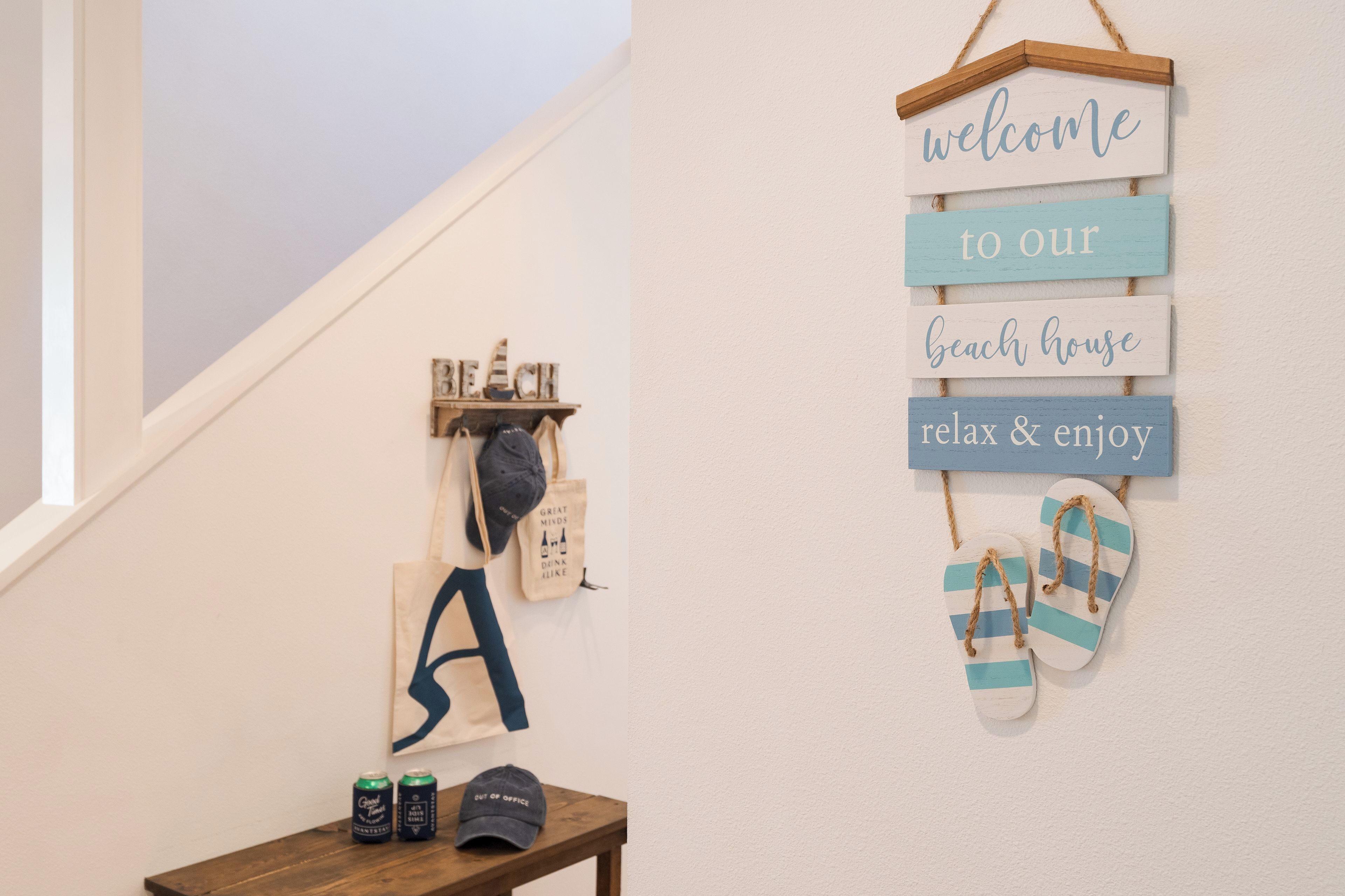 Una escalera con un cartel de bienvenida, chanclas y una mesa con gorra y latas.