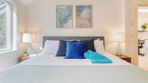 A neatly arranged bedroom with a large bed, two wall-mounted paintings, and a window providing natural light. - Walk to Beach + Relax in Hot Tub + Dine on the Deck Loli's Place by Avantstay (Arch Cape)