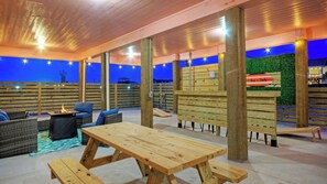 An outdoor seating area with wooden tables and chairs, a fire pit, and a view of the water.