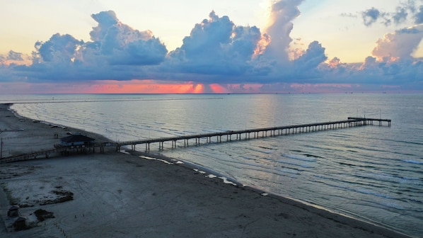 A beach with a pier extending into calm waters, a clear sky, and a sunset.