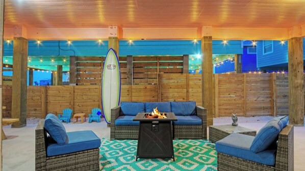 An outdoor seating area with wicker furniture, a fire pit, and a surfboard.
