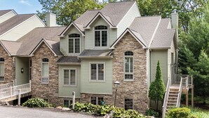 A multi-story house with stone and siding exterior, multiple windows, and a front porch with a railing.