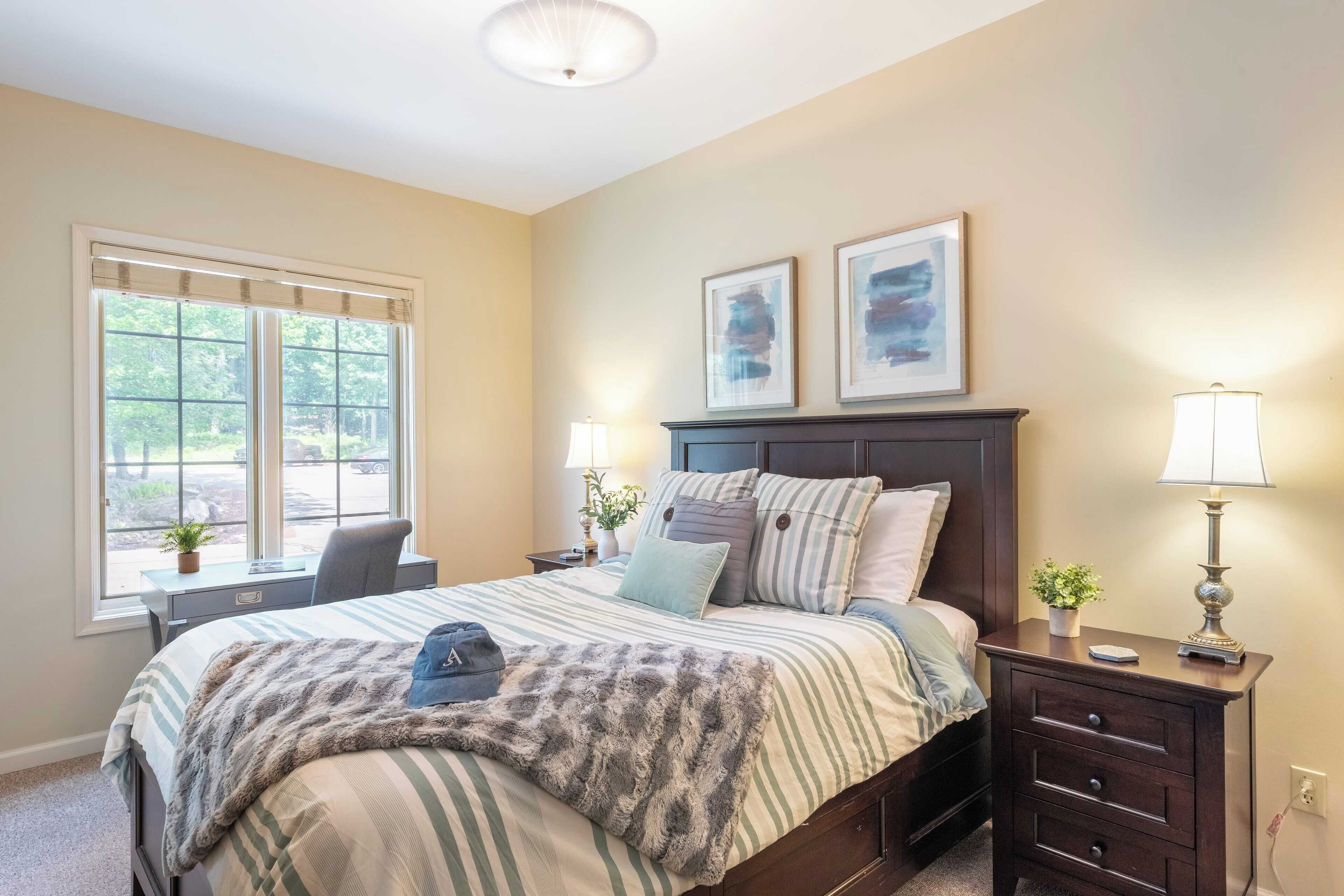 A bedroom with a bed, bedside tables, a desk, and a window.