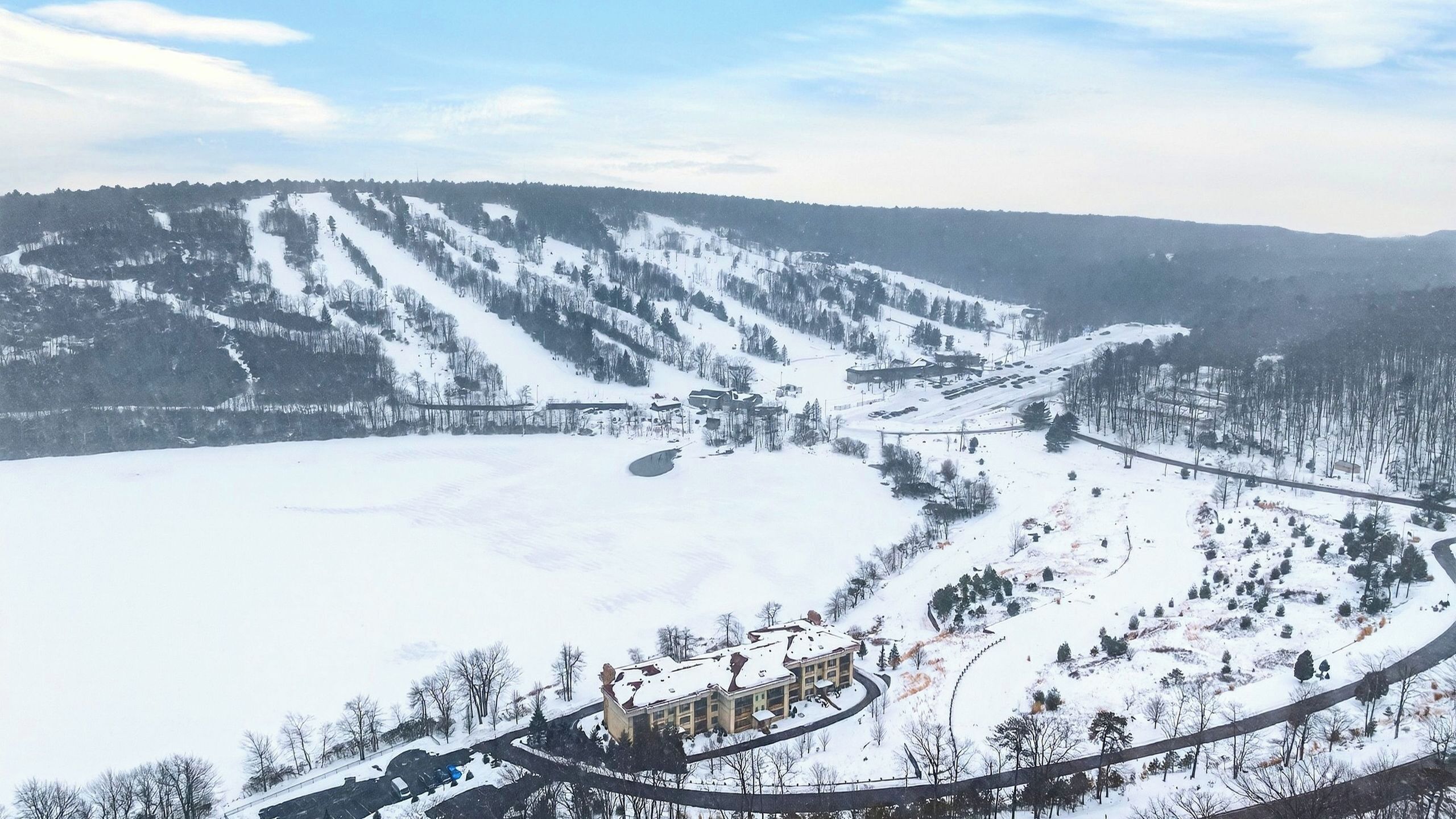 Paisatge cobert de neu amb una estació d'esquí, incloent pistes d'esquí, una estació d'ascensors i un edifici amb teulada corbada.