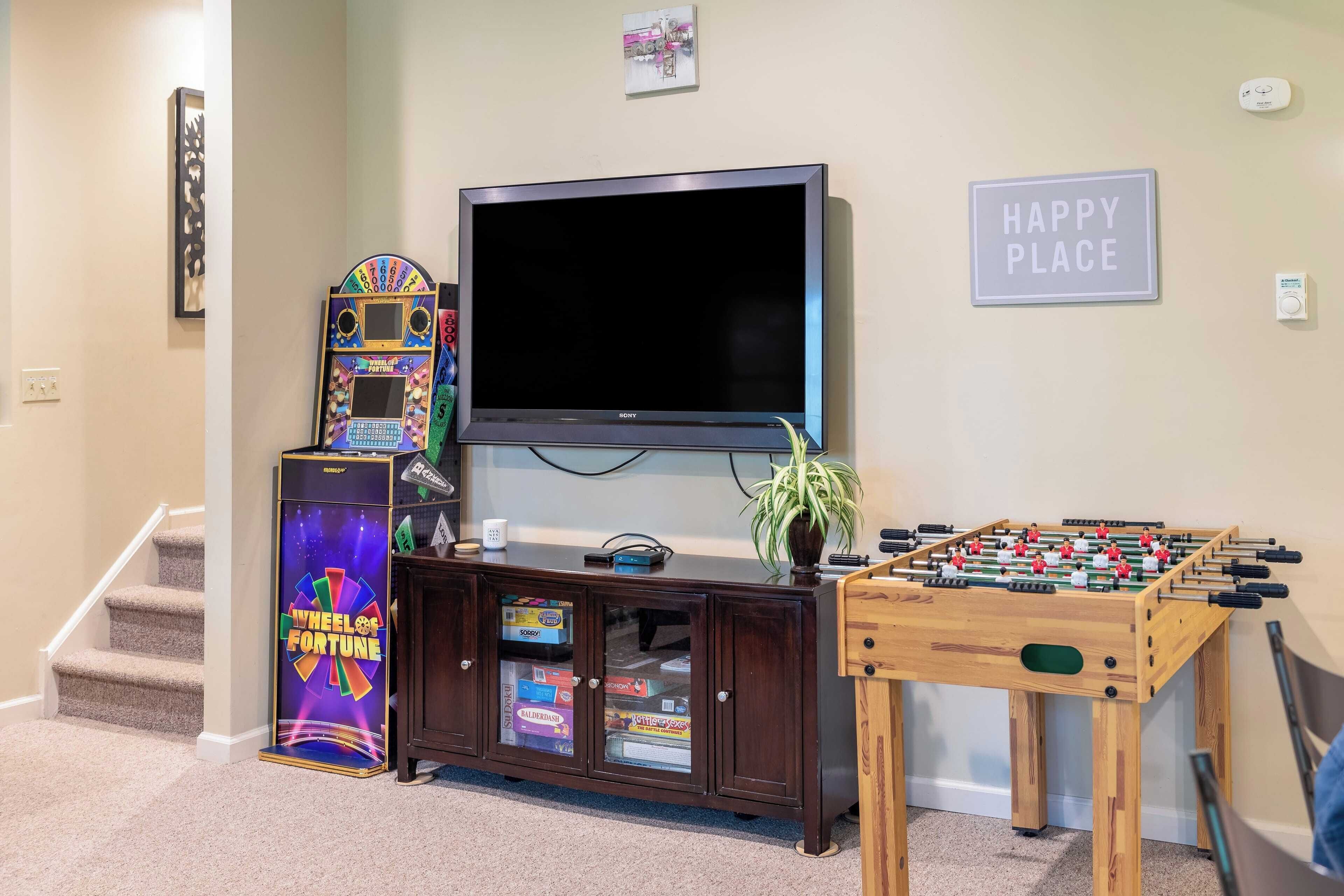 A room with a TV, a foosball table, and a cabinet with arcade games.