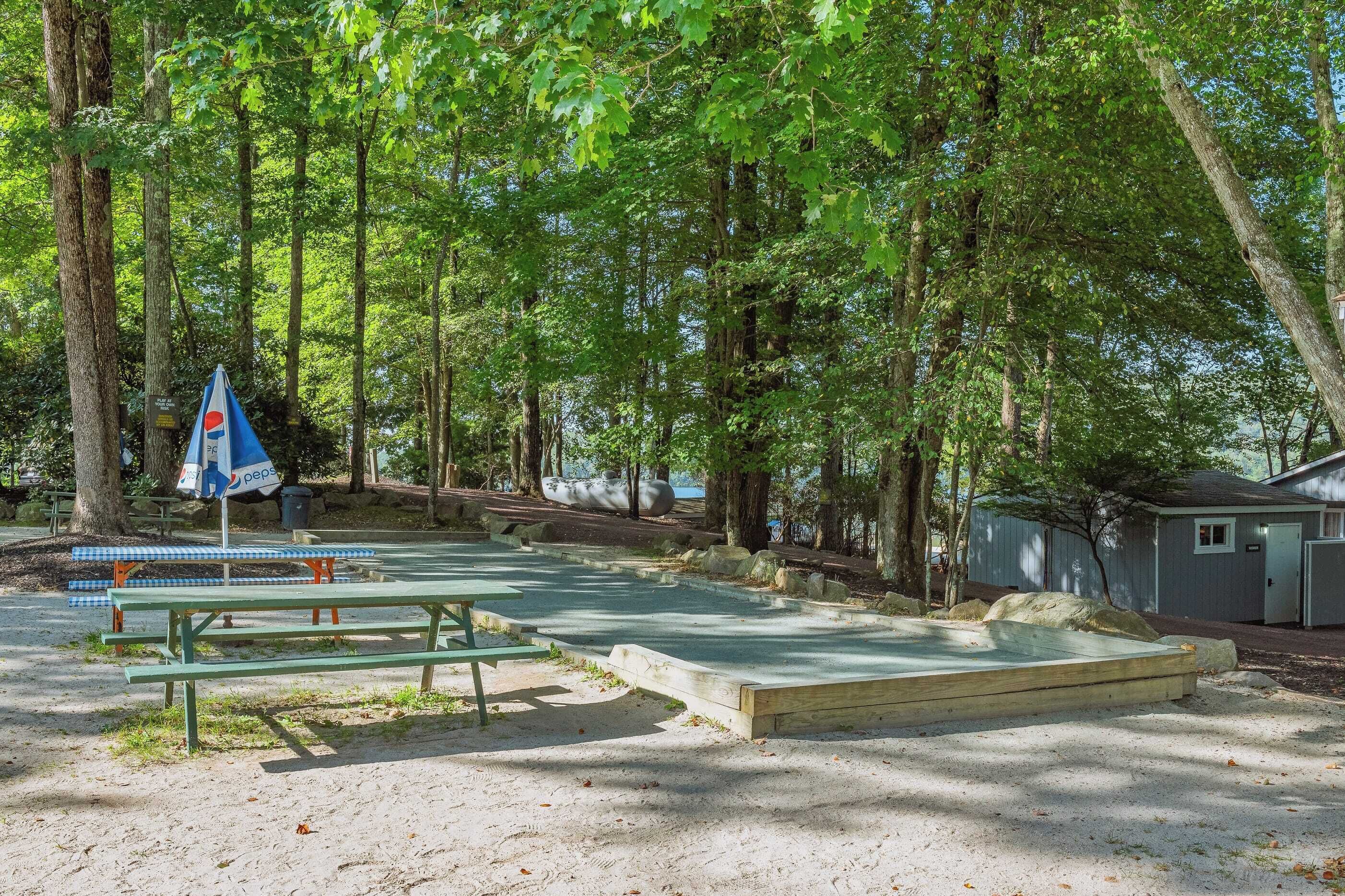 A picnic area with benches and a table, surrounded by trees and a small building.