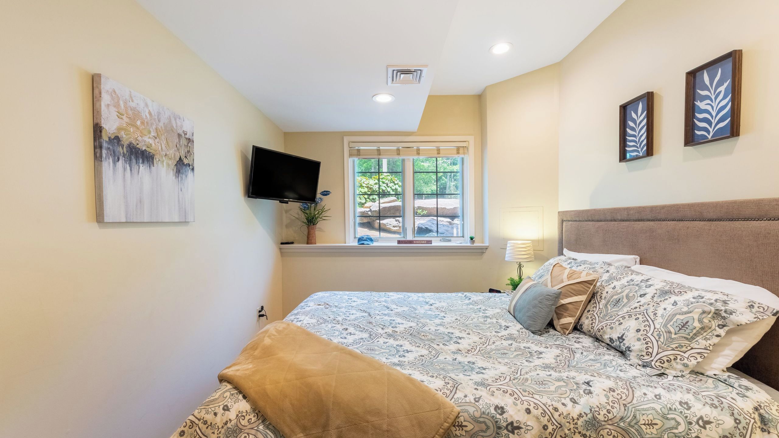 A bedroom with a bed, a window with a view, a flat-screen TV, and a painting on the wall.
