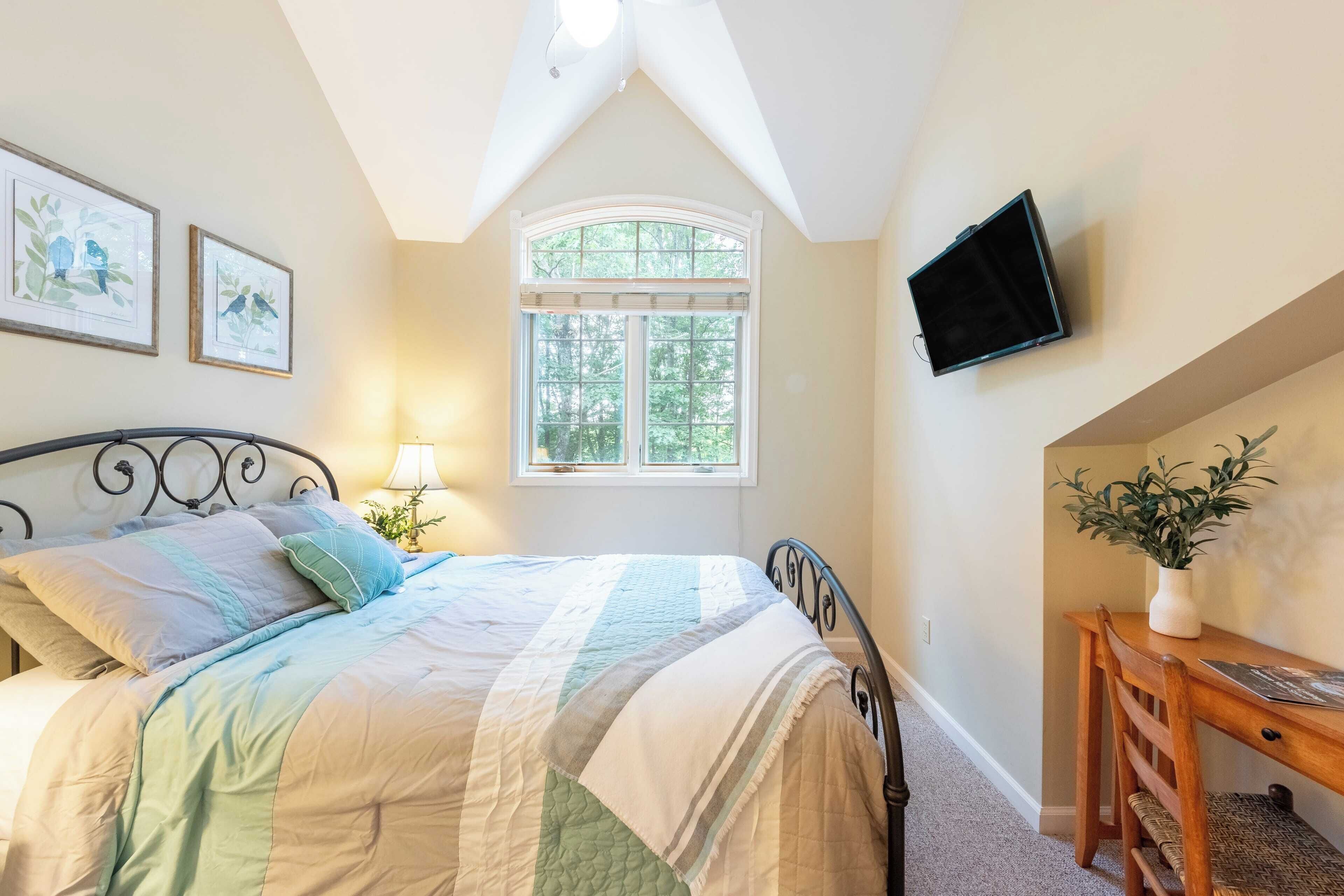 A bedroom with a bed, a window, a desk, and a television.