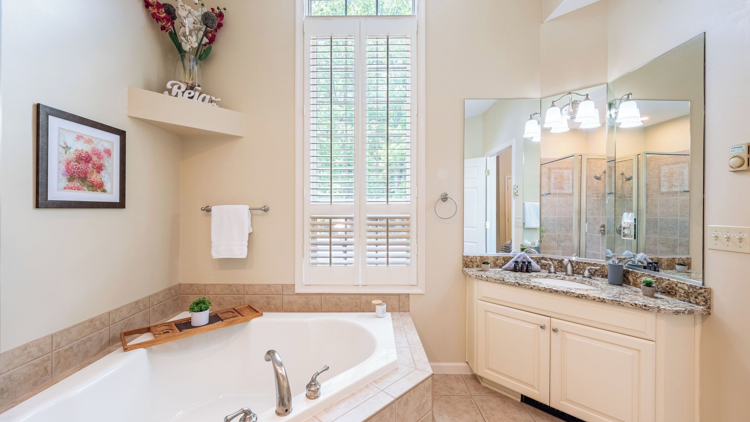 A modern bathroom with a large bathtub, a vanity with a mirror, and a window with shutters.