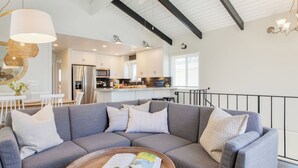 A modern living room with a sectional sofa, a dining area with a white table, and a kitchen with white cabinets and stainless steel appliances. - Surfrider II by Avantstay Walk to the Beach + Balcony (Newport Beach)