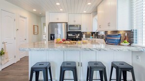 A modern kitchen with white cabinets, a marble countertop, and three black stools. - Surfrider II by Avantstay Walk to the Beach + Balcony (Newport Beach)