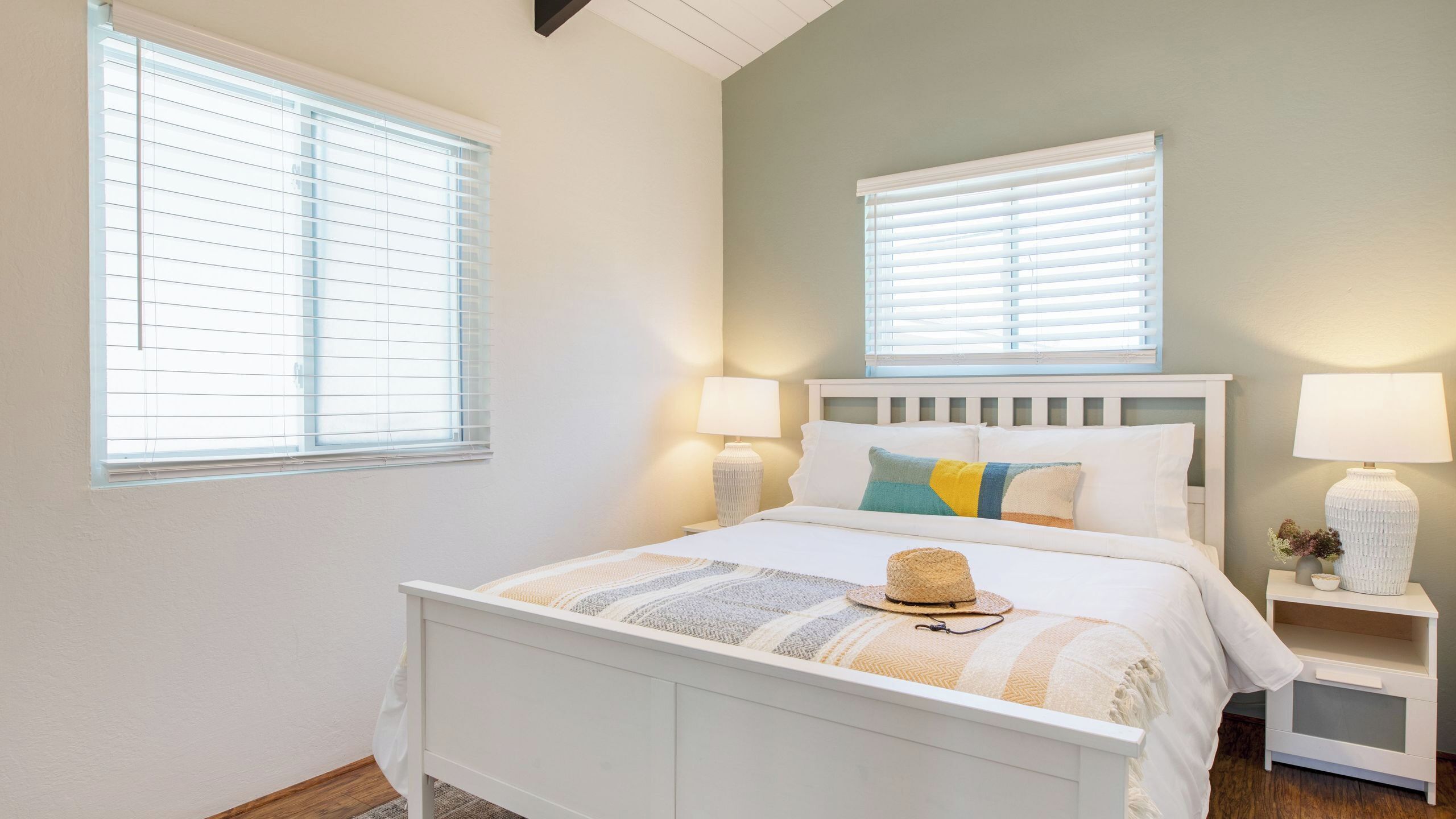 Un dormitorio con una cama, dos mesitas de noche y dos ventanas con persianas.