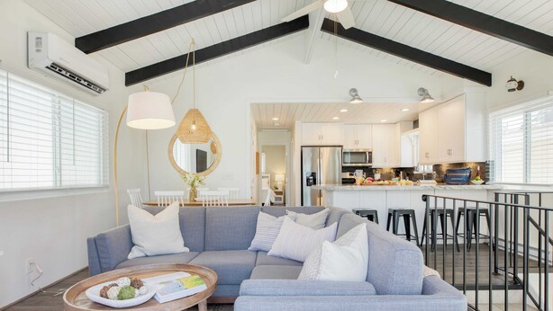 A modern living room with a grey sectional sofa, a round coffee table with snacks, and a kitchen in the background. - Surfrider II by Avantstay Walk to the Beach + Balcony (Newport Beach)