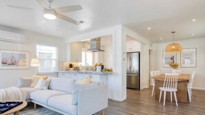 Una sala de estar moderna con un sofá gris, una mesa de centro y un comedor con una mesa de madera y sillas blancas.