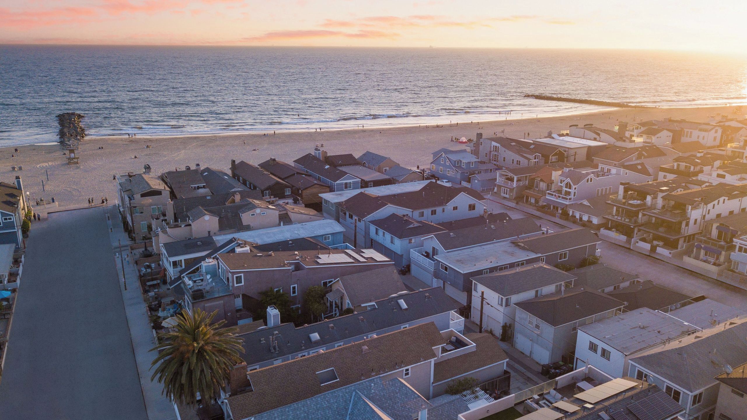 An aerial view of a coastal residential area with houses, a beach, and a clear sky.