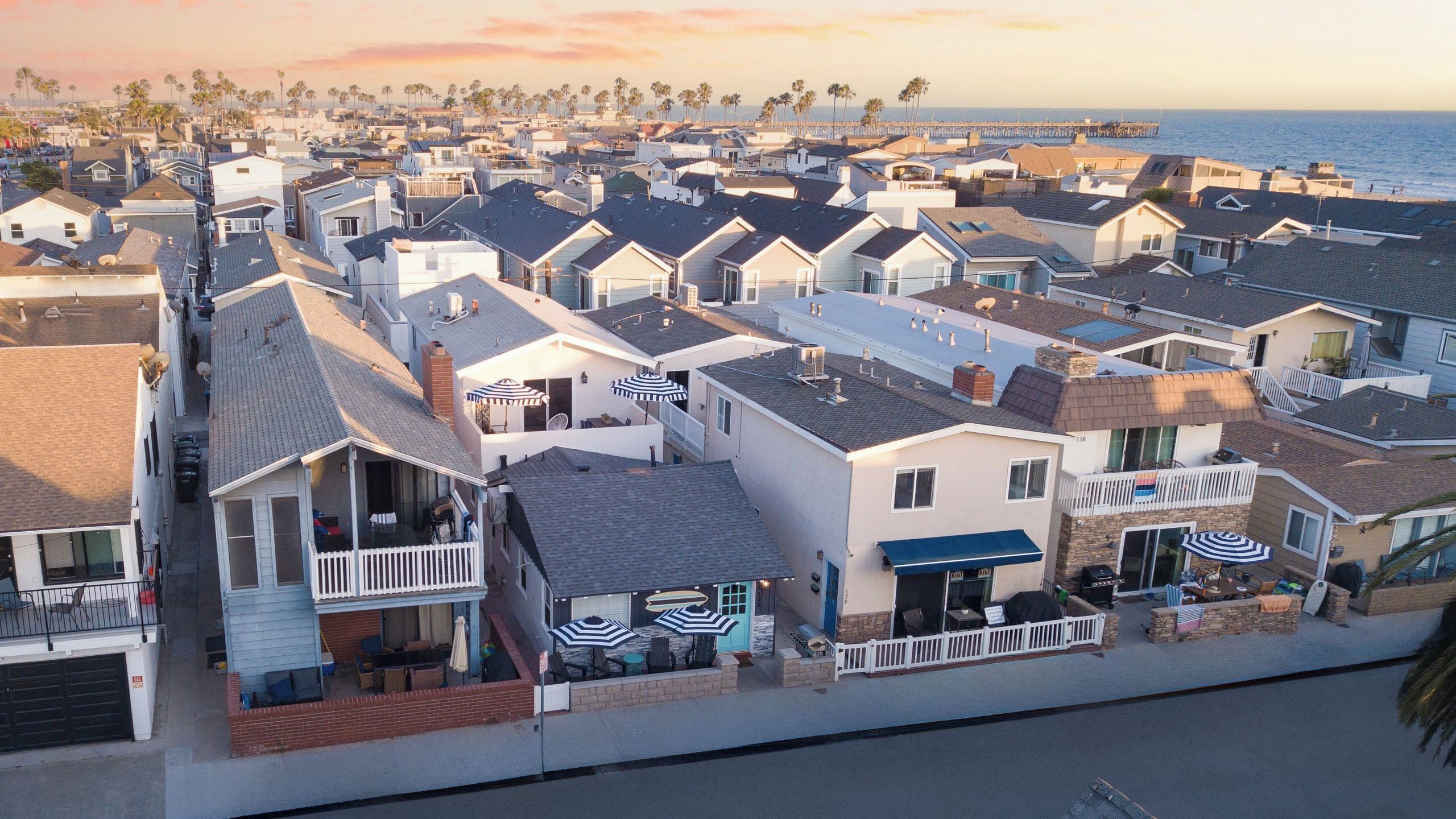 A coastal residential area with houses featuring balconies, some with outdoor seating and umbrellas, and a beach in the background.