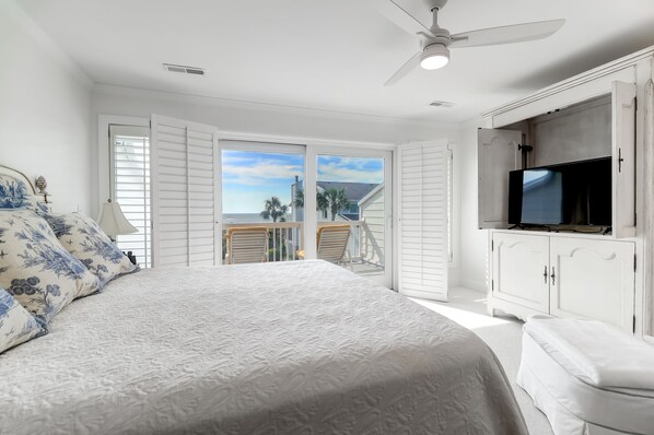 A bedroom with a large bed, a television, and a balcony with white shutters.