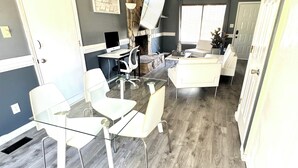 Un salon moderne avec une table à manger en verre, des chaises blanches, une cheminée et un mur d’accent en pierre.