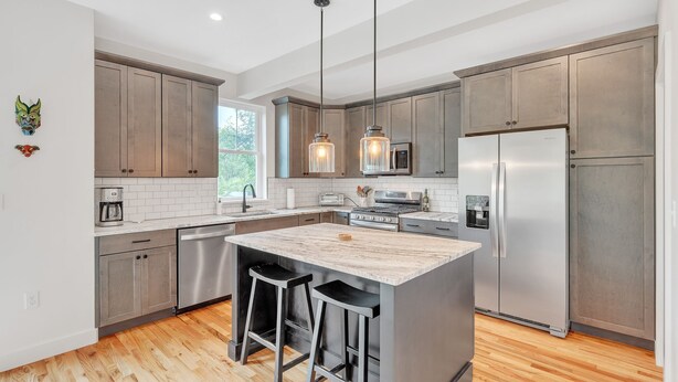 A modern kitchen with wooden cabinets, a marble island, stainless steel appliances, and pendant lighting.