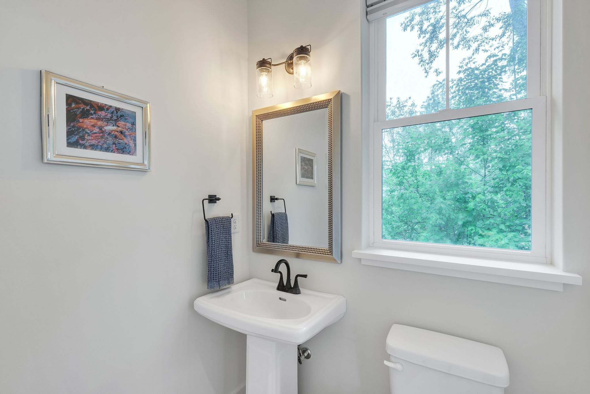 A bathroom with a white sink, a mirror with a gold frame, and a window with a view of trees.