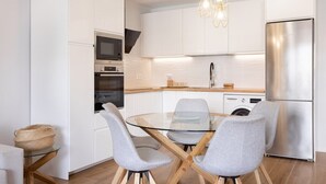 A modern kitchen with white cabinetry, a stainless steel refrigerator, a glass dining table with four grey chairs, and a hanging light fixture. - Home2Book Stylish Oasis Pool&Terrace Golf del Sur (Arona)