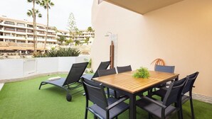 A balcony with a wooden table and chairs, a small plant, and a view of a building with palm trees. - Home2Book Stylish Oasis Pool&Terrace Golf del Sur (Arona)